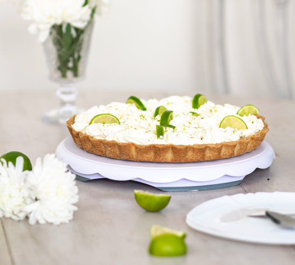Picture of lime curd tart on table, topped with cream and lime wedges