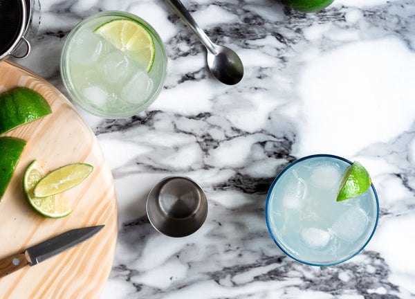 Picture of 2 glasses full of classic lime gimlet cocktail on marble table