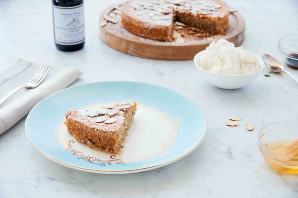 Photo of slice of Almond Torte Dessert with bottle of Vanilla Extract and fresh whipped cream on marble table