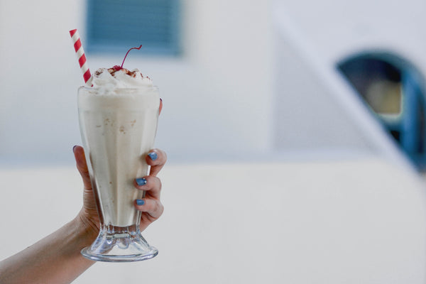 Picture of female hand holding a chocolate milkshake topped with a cherry and straw