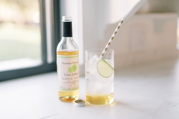 Photo of a Lime Rickey cocktail next to a bottle of our Lime Simple Syrup.
