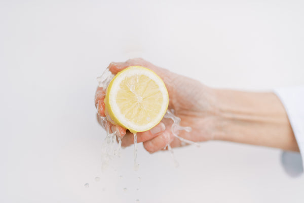 Picture of fresh meyer lemon being squeezed with hand, dripping down juice for Lemon Drop Cocktail