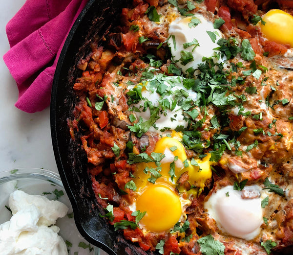 Photo of a cast iron pan filled with a delicious shakshuka with runny egg yolks and cilantro on top.