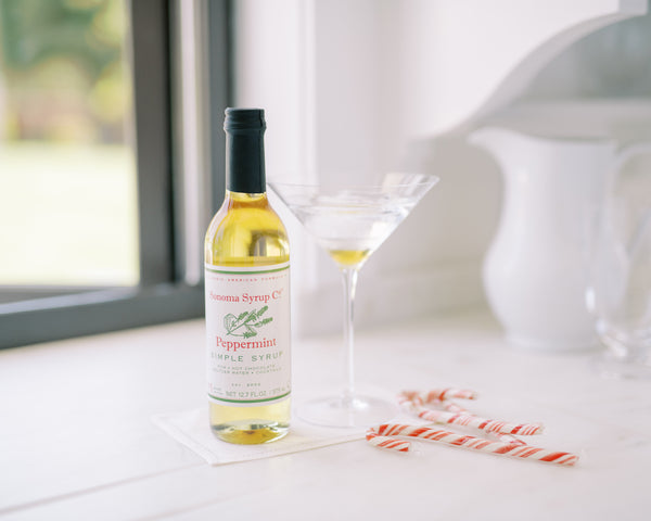 Peppermint Martini with candy canes and a bottle of Sonoma Syrup Co. Peppermint Simple Syrup