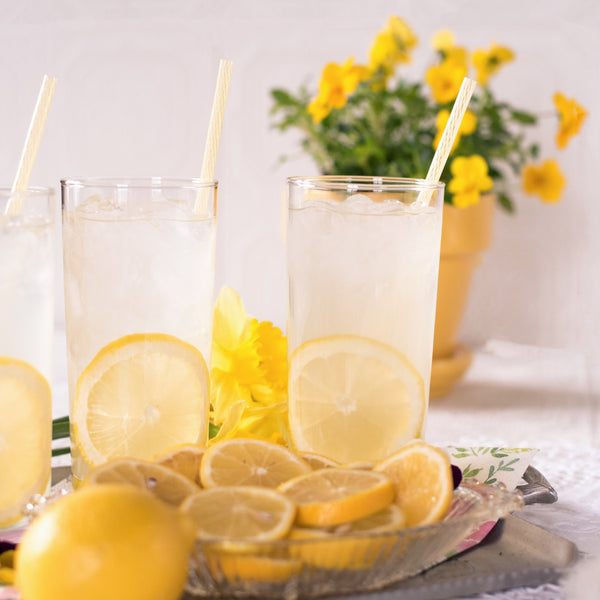 Brightly yellow photo of three glasses full of lemonade with a slice of lemon and lemon straw.