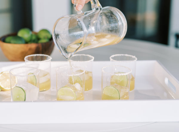 Picture of 6 cocktail glasses on a tray filled with margarita cocktails and a pitcher pouring into a glass