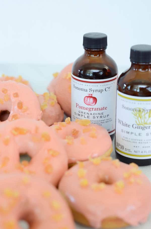 pile of pink glazed-doughnuts topped with crystalized ginger with extract bottle in background